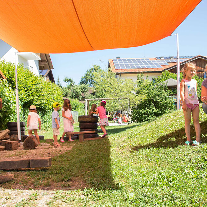 Kinder spielen im Schatten eines Sonnensegels an einem sonnigen Tag.