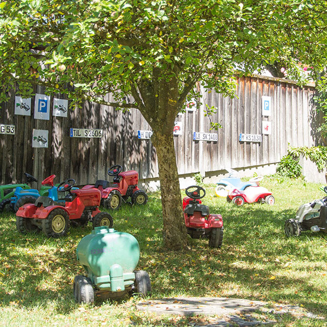Der Fuhrpark von Tretfahrzeugen für die Kinder in der KiTa Eurasburg, mit Parkplatz Schildern im Hintergrund.