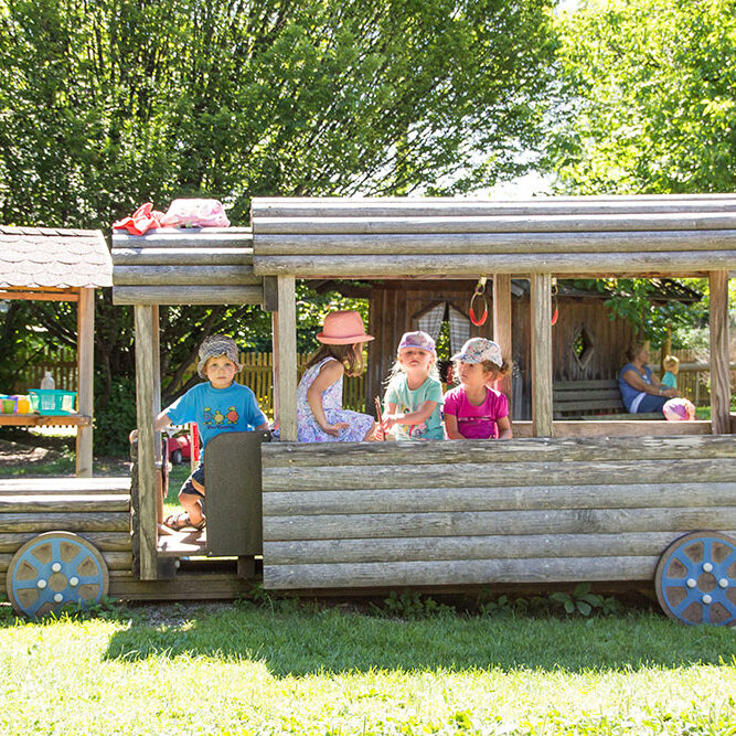 Kinder beim spielen im Garten der KiTa Eurasburg in einem hölzernen Bus.